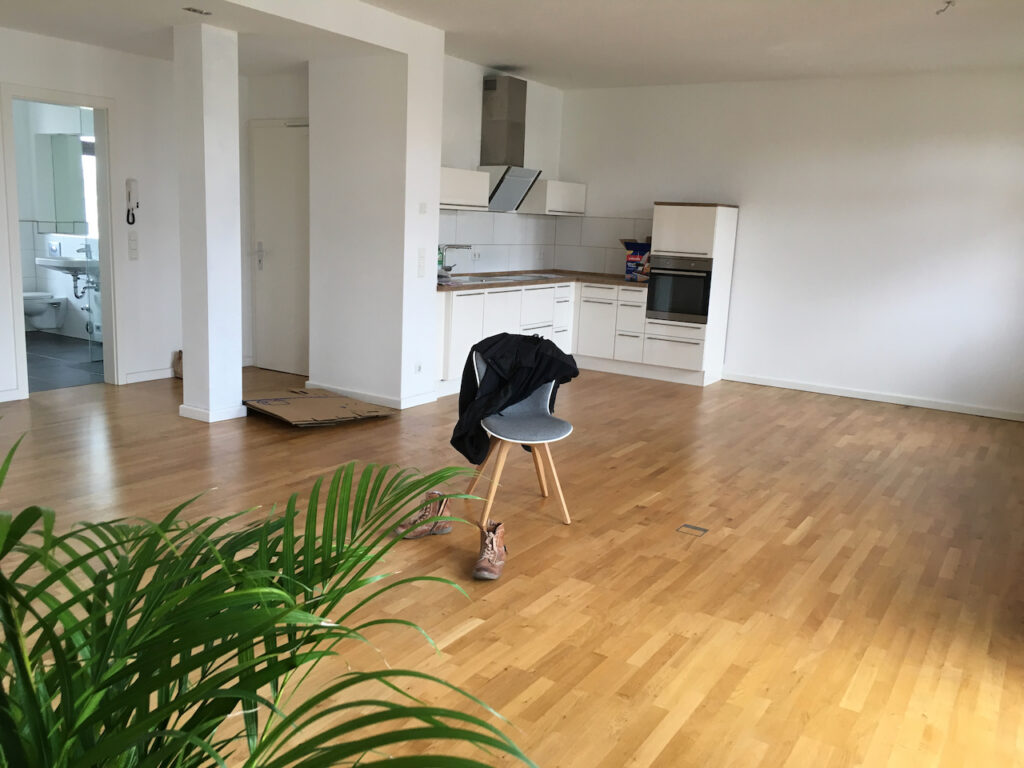 Stanza spoglia con parquet e una sola sedia davanti alla finestra chiusa