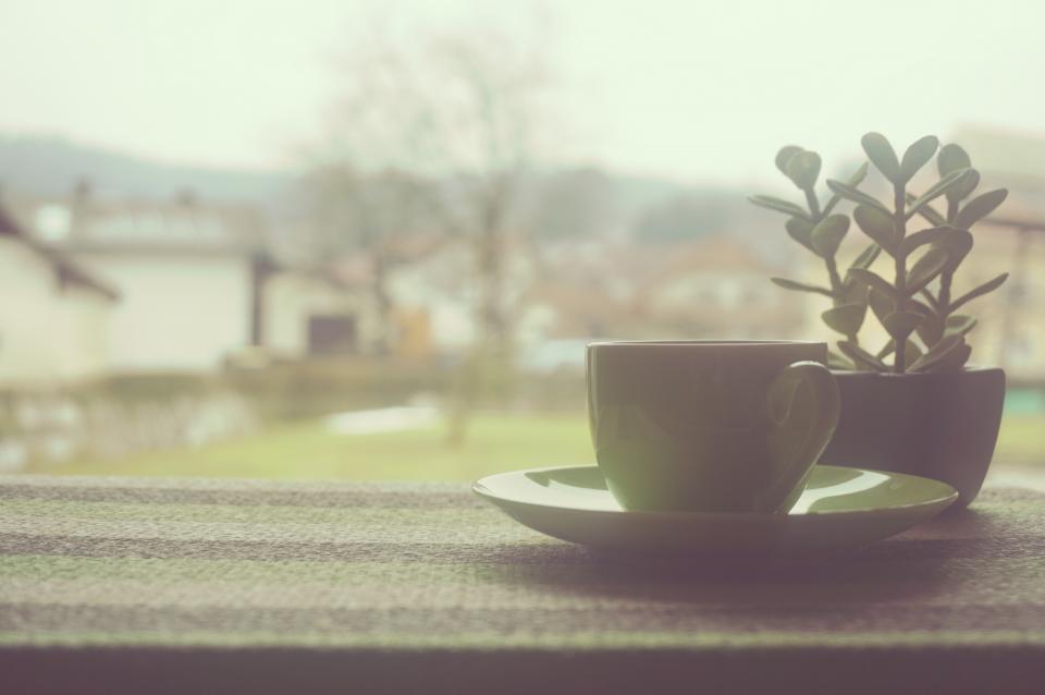 Tazza di caff&egrave; appoggiata accanto a un quaderno aperto su un piano di lavoro