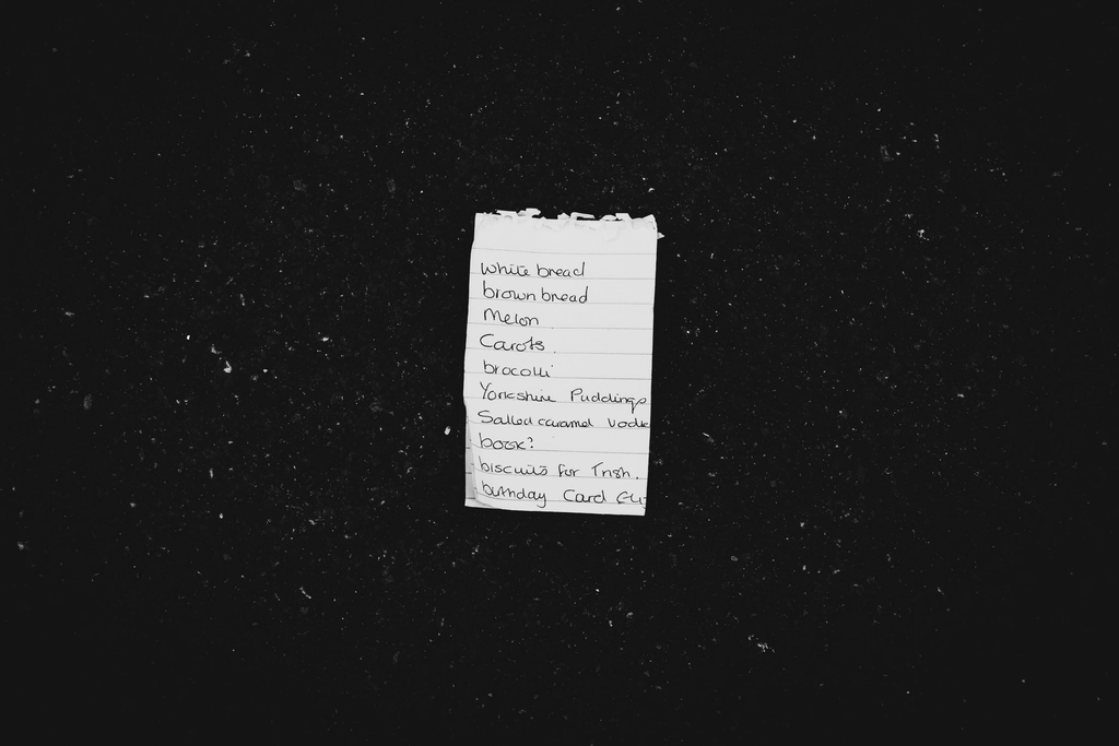 Lista della spesa scritta a mano su un foglio appoggiato al piano di una cucina